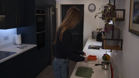 Plano-General-De-Una-Modelo-Femenina-Preparando-Comida,-Cortando-Zanahorias,-Luego-Colocándolas-En-Una-Sartén-Y-Caminando-En-Una-Cocina-Moderna