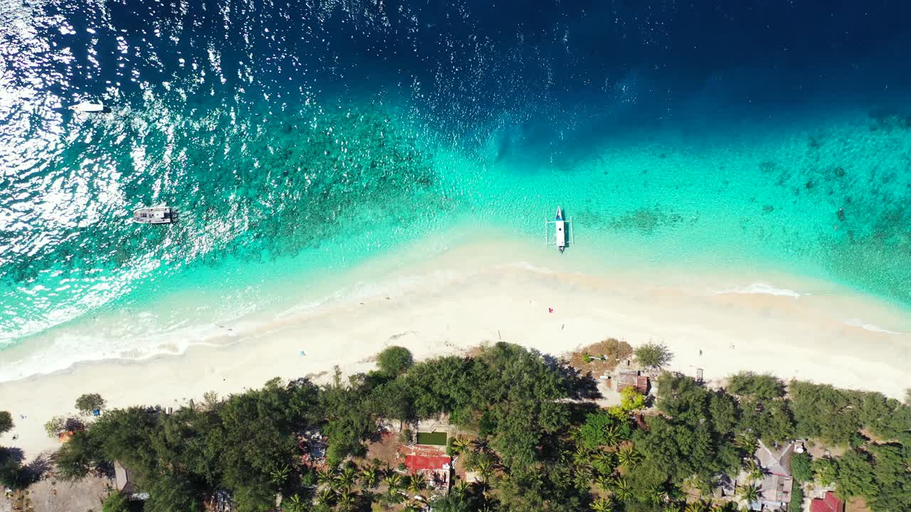 Splendida spiaggia tropicale con sabbia bianca bagnata dalle acque turchesi e blu di una laguna calma che riflette la luce del sole, con barche ancorate di fronte a hotel per vacanze.