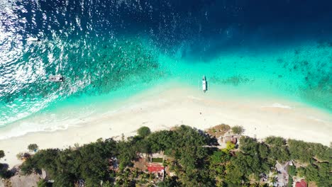 beautiful tropical beach with white sand washed by blue turquoise water of calm lagoon reflecting sunlight, boats anchoring in front of holiday hotels