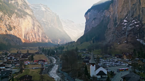 drone ascends above calm town in lauterbrunnen, switzerland in the shadow of canyon walls