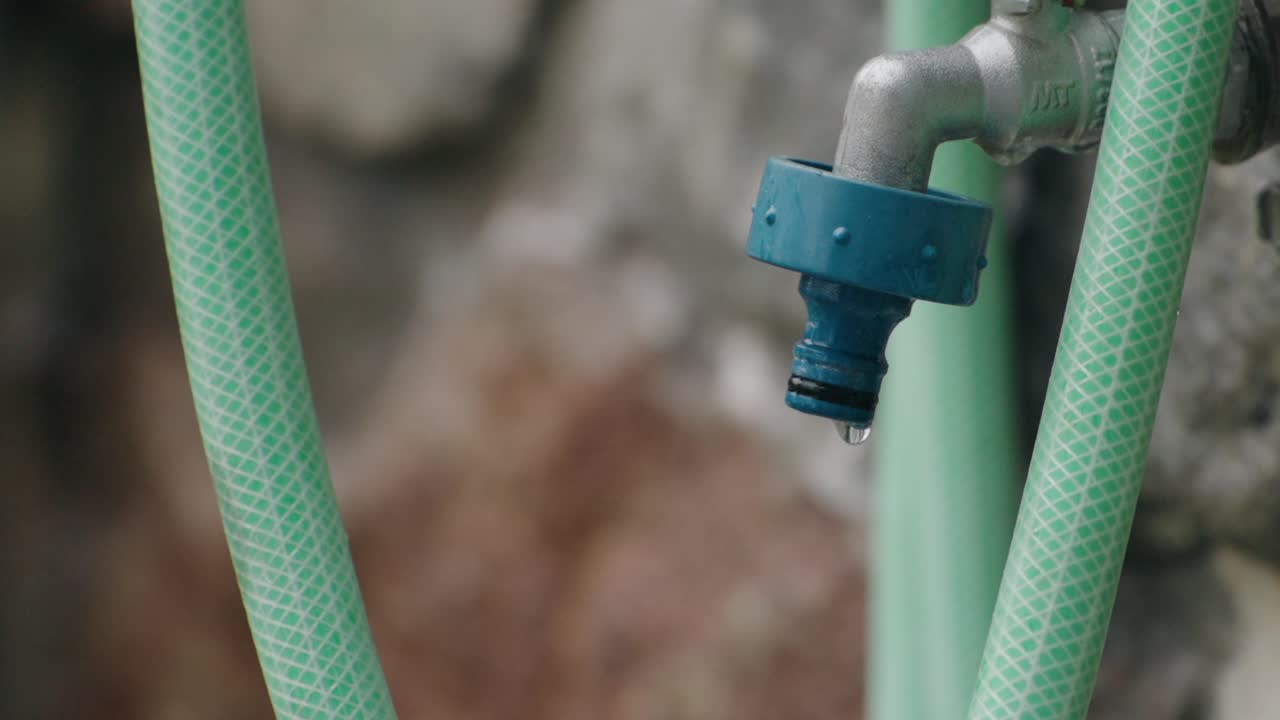 Close up of outdoor faucet with blue hose connector and water dripping slowly