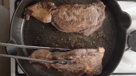 steaks seared and flipped in a cast iron skillet with oil - overhead view