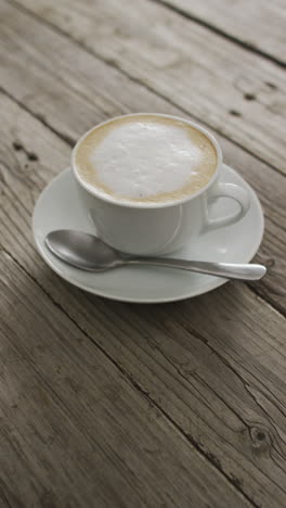 video vertical de una taza de café capuchino con leche espumada en una mesa de madera