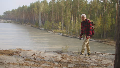 middle-aged fisherman is walking over high shore of reservoir or natural lake in forest angling in freshwater relax and recreation