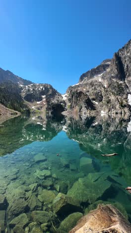 Vista-Vertical-Del-Lago-Con-Aguas-Cristalinas-De-Color-Esmeralda-Con-Reflejo-De-Colinas-Rocosas,-Panorama