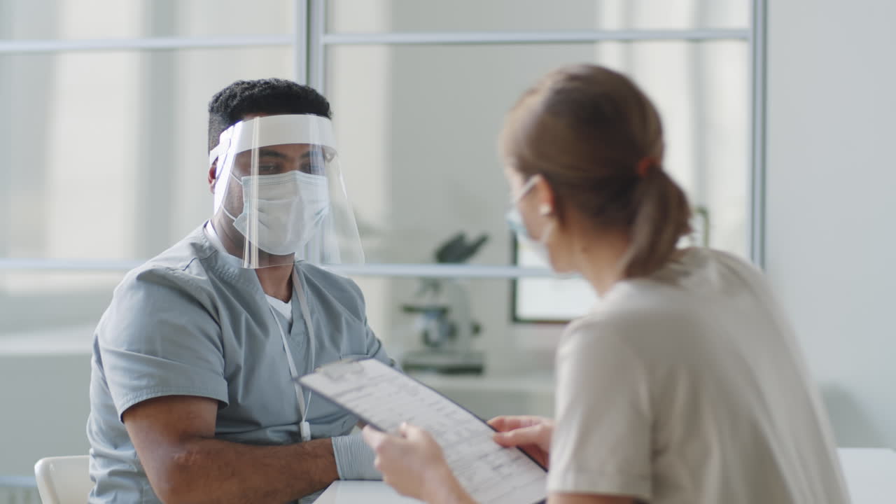 médico en uniforme de protección hablando con una paciente femenina
