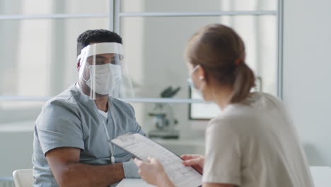 Médico-Con-Uniforme-Protector-Hablando-Con-Una-Paciente