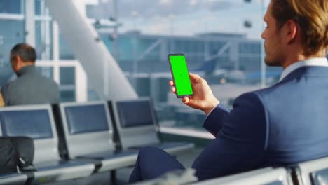 terminal del aeropuerto: hombre de negocios trabajando en una pantalla clave de croma verde teléfono móvil, espera un vuelo de avión. empresario hace trabajo remoto en línea en la sala de embarque del centro de la aerolínea. por encima del hombro
