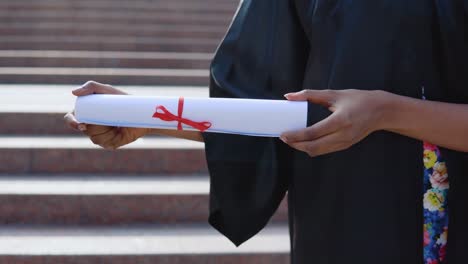 diploma of higher education horizontally in the hands of an african-american female university graduate on the background of the stairs from the outside.