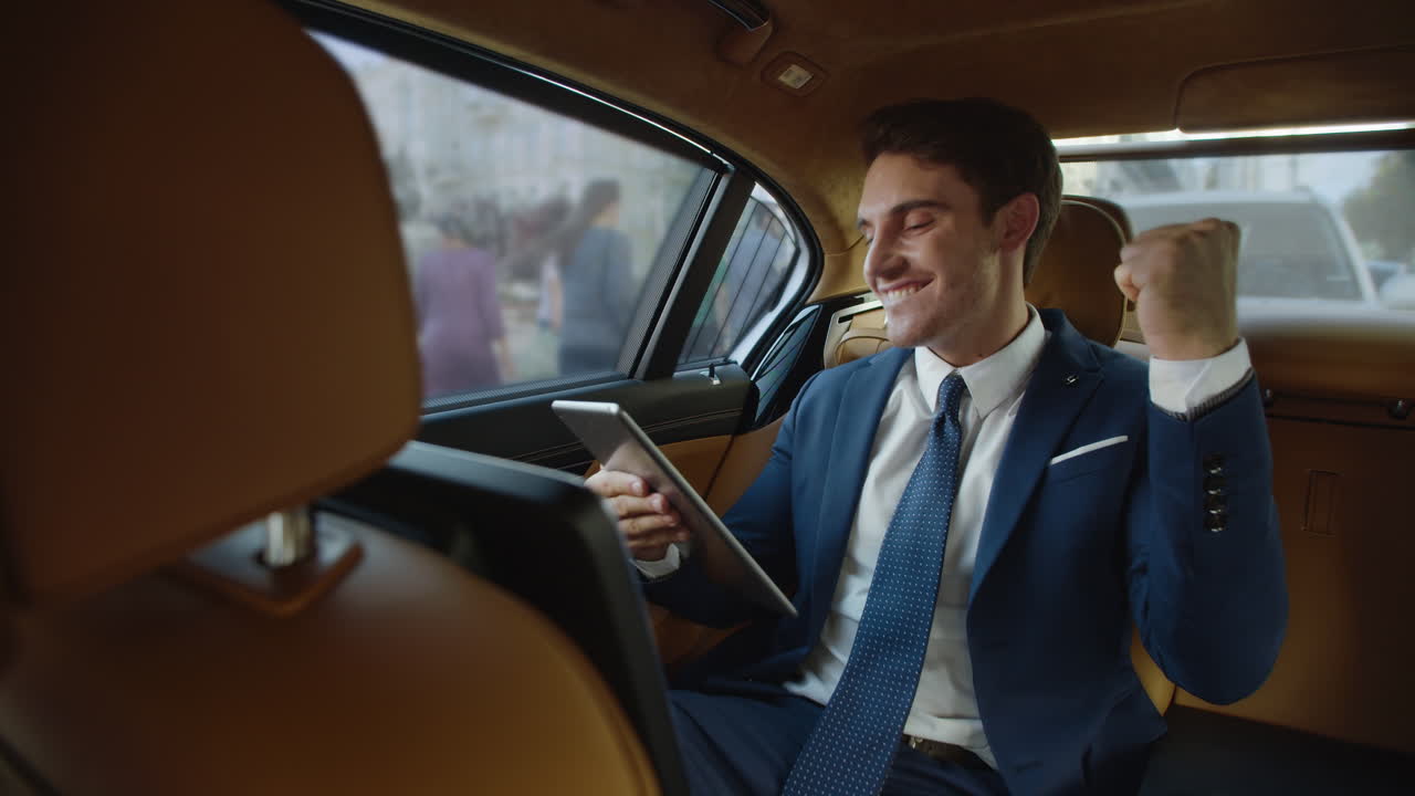 hombre profesional feliz leyendo excelentes noticias en una tableta en un coche moderno.