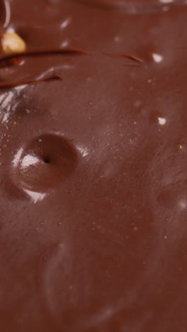 vertical video close up overhead shot of pieces of chocolate and hazelnuts being dropped into melted chocolate sauce