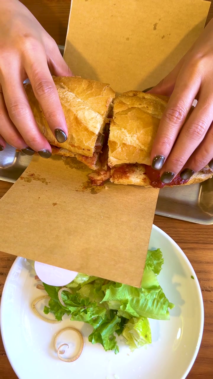 Top-down view of hands unwrapping a crusty Vietnamese baguette sandwich served with fresh green salad