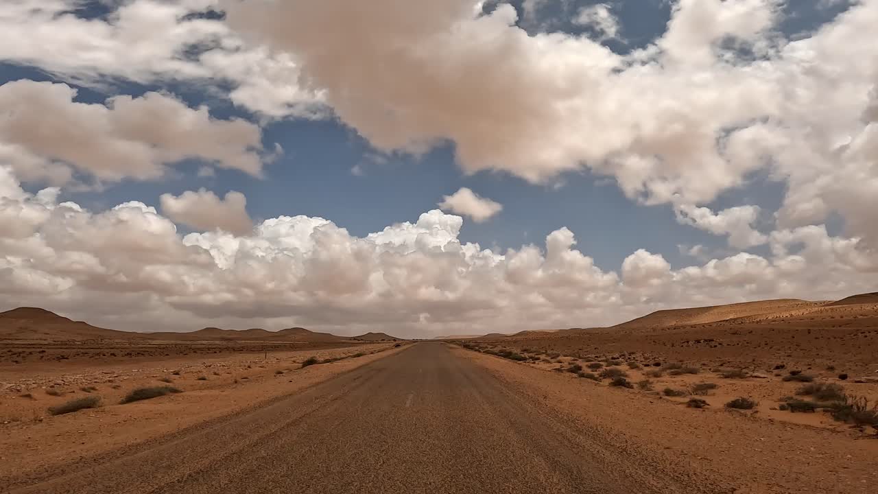 Guida su una strada desertica attraverso un paesaggio arido con nuvole bianche nel cielo blu.