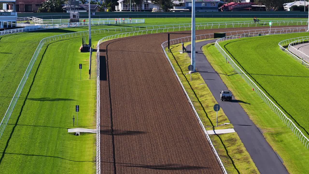 High-angle drone footage glides above a sunlit, empty horse racing track curve in Gold Coast, Australia, highlighting vibrant green turf and clear weather