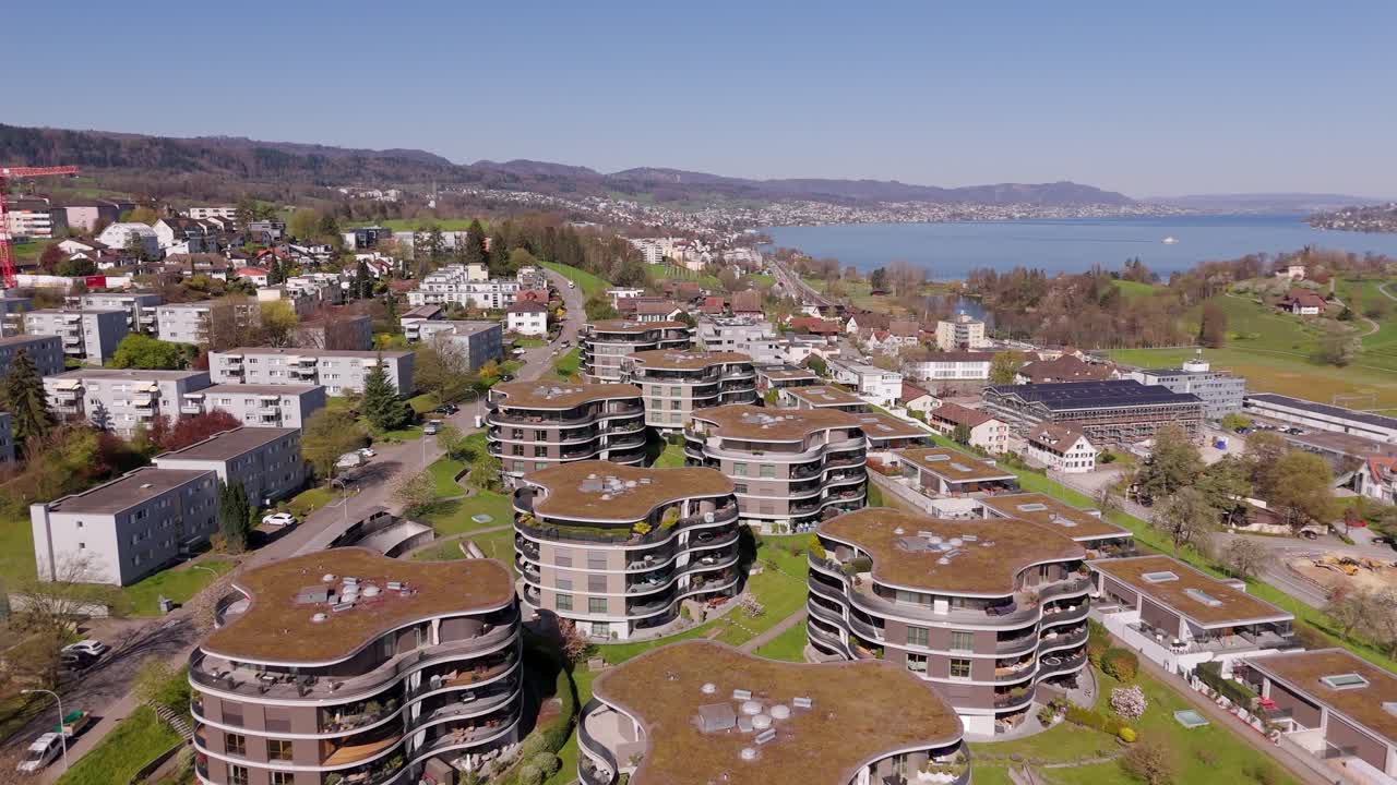 Modern architectures with green rooftop during sunny day in Switzerland. Luxury apartment houses and Lake Zurich in background. Wädenswil, Switzerland. Aerial forward wide shot.
