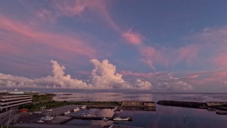 static time-lapse shot of cumulonimbus clouds billowing towards the stratosphere, over the ocean while being illuminated from a deep pink through orange to yellow as the sunrises