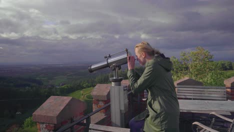 A-blonde-girl-walking-towards-a-telescope-from-a-patio-which-belongs-to-a-castle-on-top-of-a-mountain