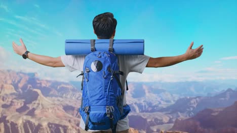 back view of a male hiker with mountaineering backpack spreading arms and looking the view around while traveling at the top of mountain