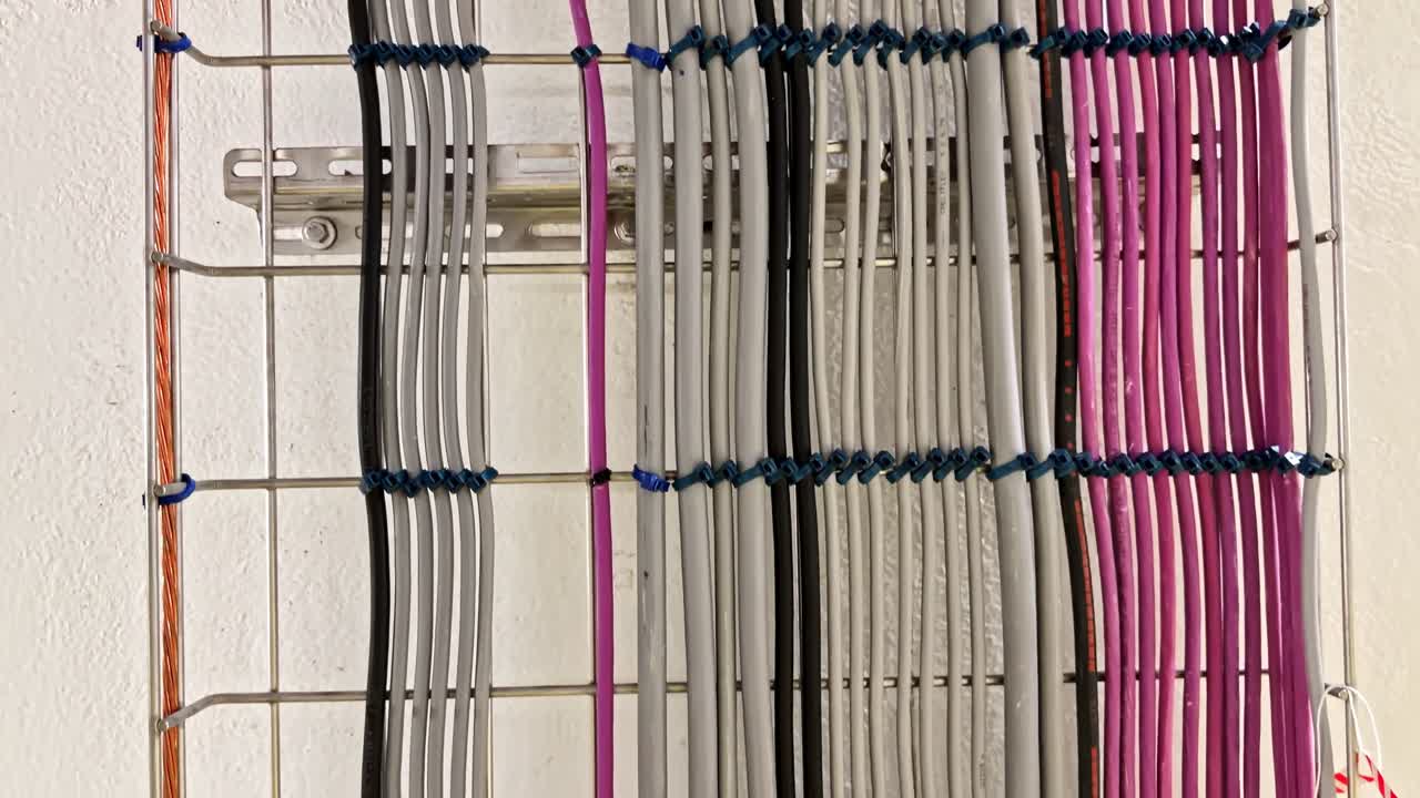 Et velordnet arrangement af elektriske kabler i flere farver, fastgjort og justeret på en metalramme mod en hvid væg – nærbillede.