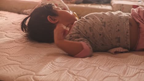 Close-up-shot-of-sleepy-asian-baby-girl-with-dummy-in-mouth-in-bed