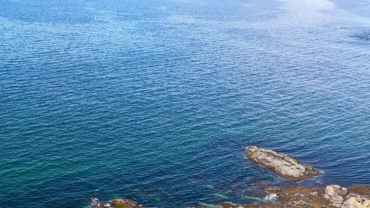 Drone si alza sopra un faro scozzese, costa rocciosa, tende e oceano blu sotto la luce del giorno