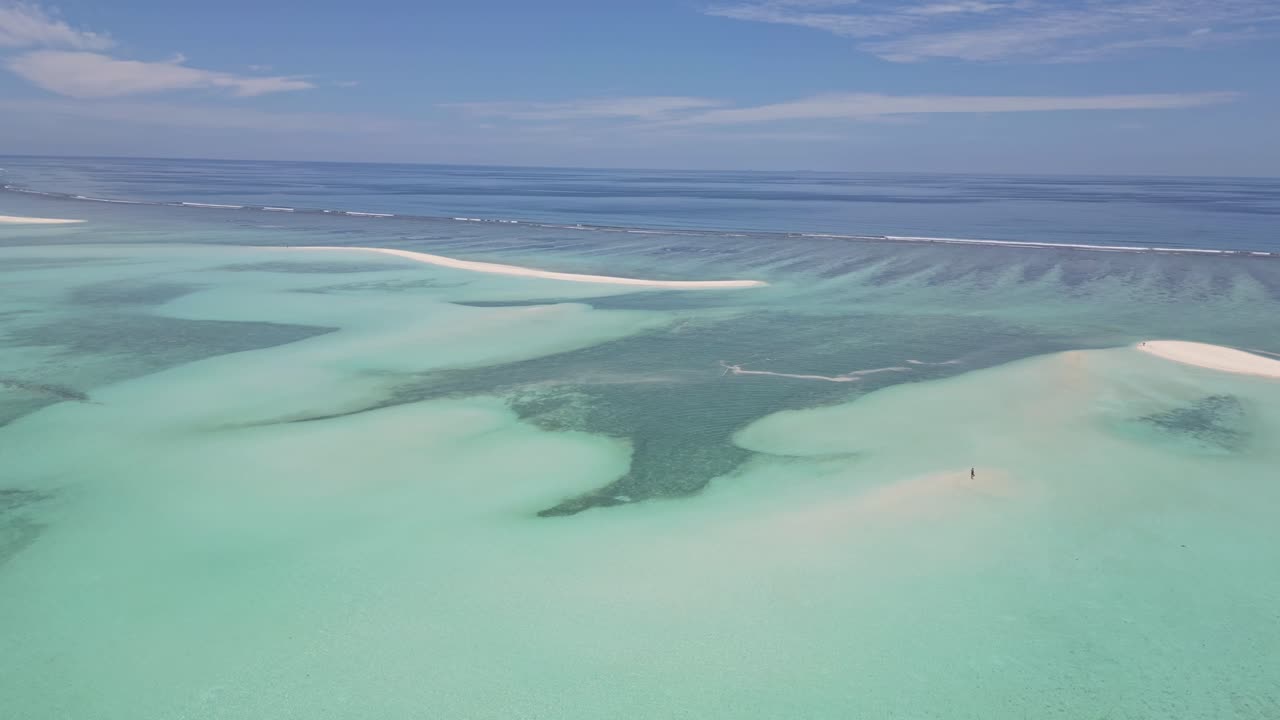 White sandbanks and shallow, crystal-clear turquoise waters in the Maldives, with a lone person walking in the distance.