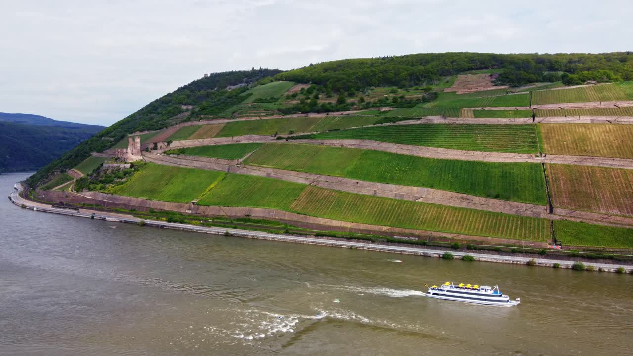 Tour boat cruising up Rhine River with Ehrenfels Castle ruins on bank, aerial