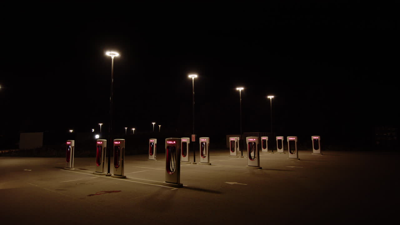Tilt-down wide shot of deserted Tesla charging stations illuminated at night