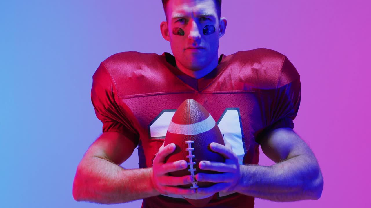 Video ritratto di un giocatore di football americano caucasico con palla su sfondo viola neon
