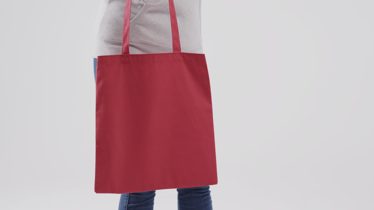 mujer caucásica con capucha blanca sosteniendo una bolsa roja sobre fondo blanco, espacio de copia, cámara lenta