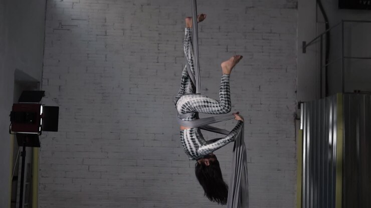 Woman circus artist practicing an aerial silk acrobatic exercise at her studio