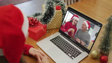 Caucasian-woman-on-video-call-on-laptop-with-female-friend-and-senior-father-at-christmas-time