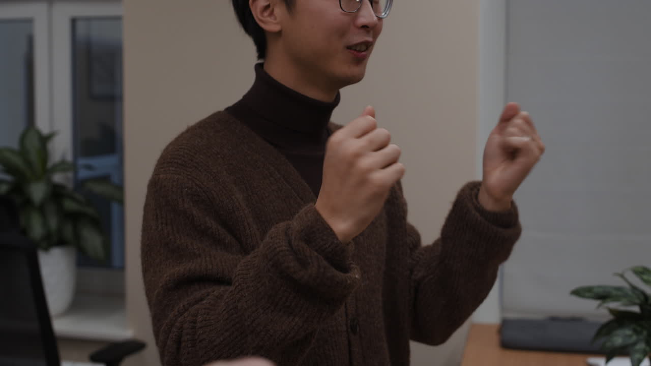 A man with glasses wearing a brown sweater and turtleneck is having a conversation