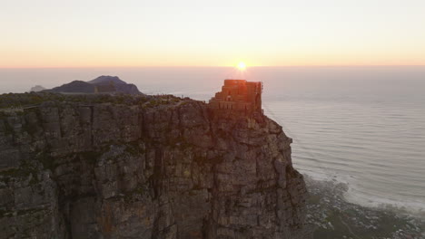 Aerial-footage-of-Table-Mountain-flat-summit-with-upper-station-of-cable-car.-Fly-around-high-rock-above-ocean-coast-at-sunset.-Cape-Town,-South-Africa