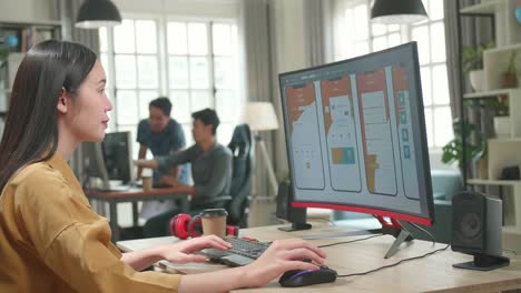 Asian Female Mobile Application Developer Works With Graphics On Her Personal Computer In Office. She Turns And Warmly Smiles Into The Camera