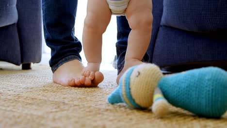 father helping his baby boy to walk in living room 4k