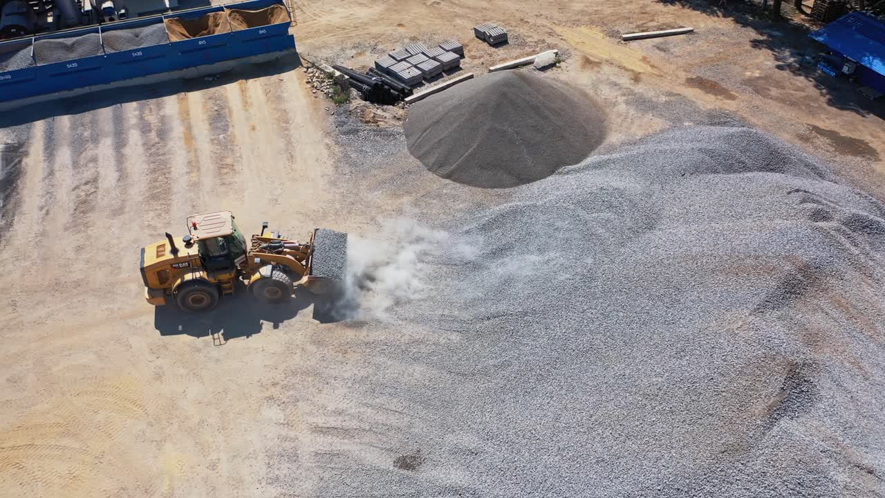 Asphalt plant with running bulldozer. The plant serves the needs of road construction. Industrial machine is loading rubbles. Aerial view.