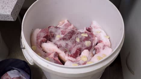 Salted-pieces-of-pork-inside-white-bucket,-motion-view