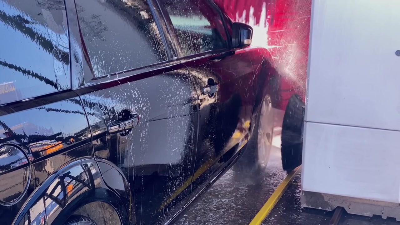 Veículo preto sendo limpo em uma estação de lavagem automática de carros. Água com sabão pulverizando na carroceria do carro.