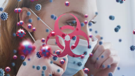 animación de células de virus y símbolo de peligro biológico sobre mujer caucásica con máscara facial