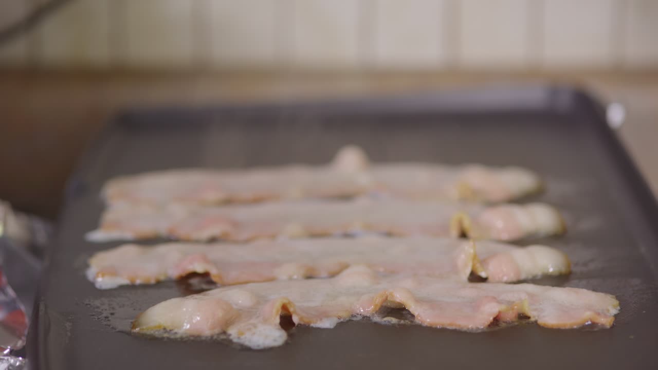 Close up of raw bacon cooking on a griddle