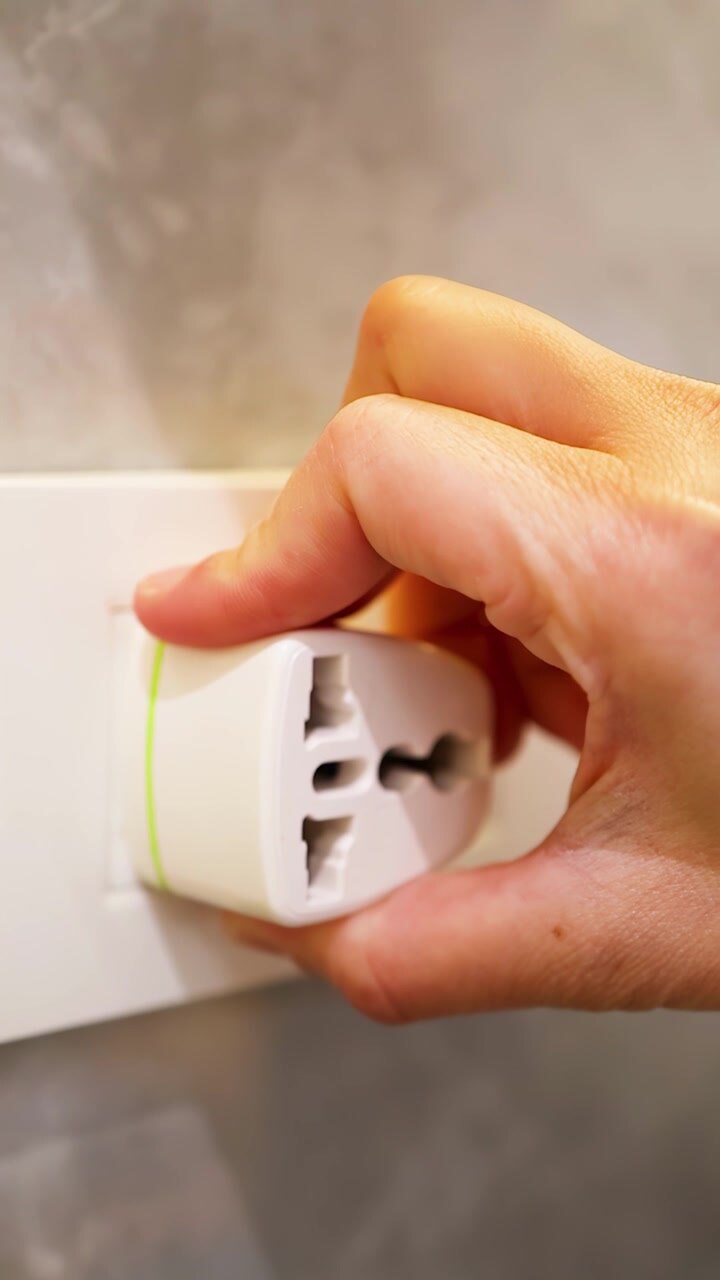 La mano di una persona rimuove un adattatore da viaggio universale bianco da una presa di corrente a muro