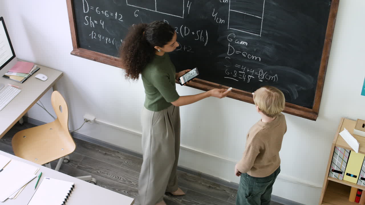 Teacher assisting student with math problem at the blackboard