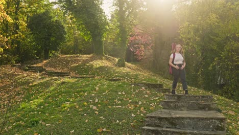 young woman, guitar case descends parkland steps, autumn sunshine