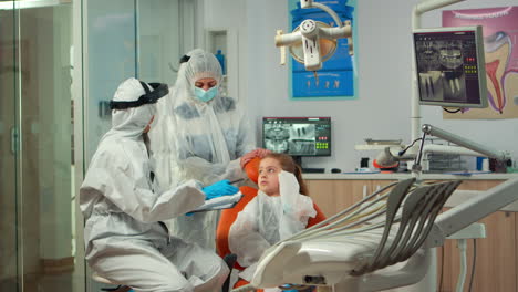 pediatric dentist and nurse in ppe suit interrogating kid patient