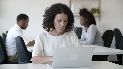 focused mature woman working with laptop in office