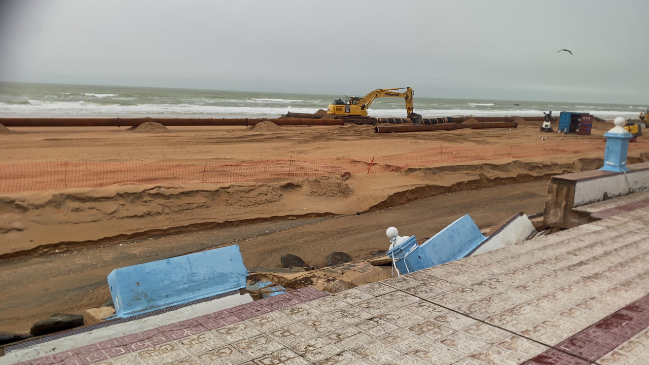 Matalascanas beach showing coastal erosion impacting the promenade after a storm, with an excavator on the sand for dredging work