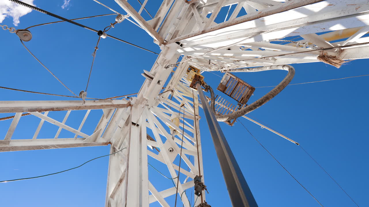 Rotating pole is attached to the white metal tower. Low angle view on the drilling equipment working outdoors.