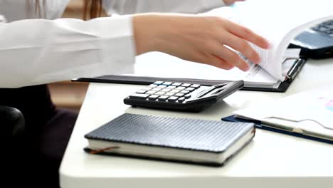 manos de la mujer contando en la calculadora y llenando documentos en la oficina moderna