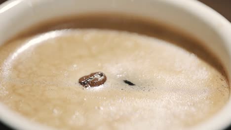 coloque un grano de café en una taza de café caliente con vapor ligero a cámara lenta